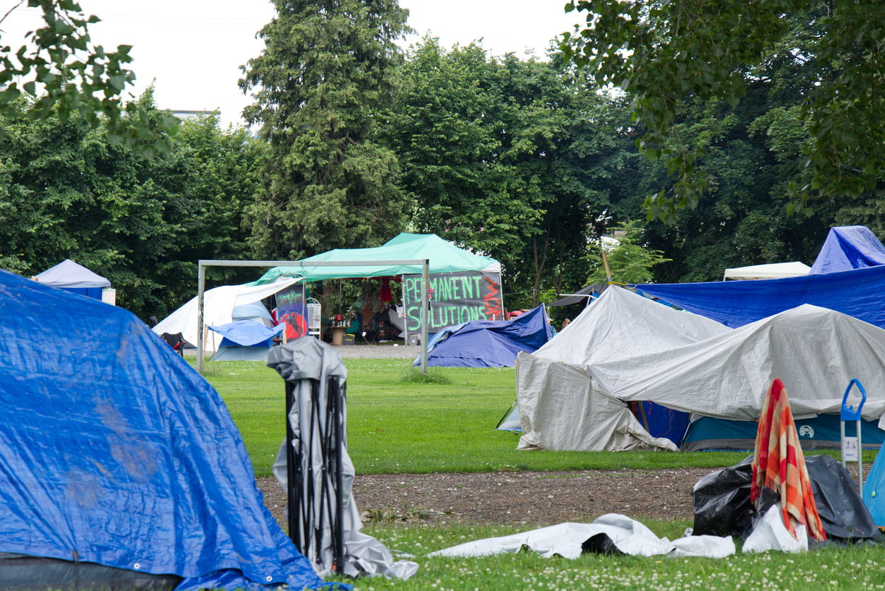 Vancouver, Canada - July 4, 2020: View of Strathcona Park in downtown Vancouver full of tents and homeless people with sign "Permanent solutions now" in the background
