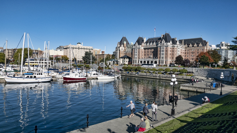 Horizontal image of sailboats, and pleasure craft moored in the Victoria Inner Harbor.  The Empress Hotel is visible in the background.  People can be seen walking along the lower causeway.