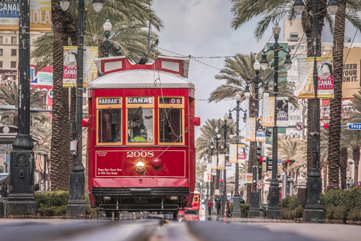 New Orleans, USA - October 05, 2016 : Famous streetcars of New Orleans driving in Canal Street during a bright spring day.  people are running along the railway which is very beautiful and filled with aligned palms