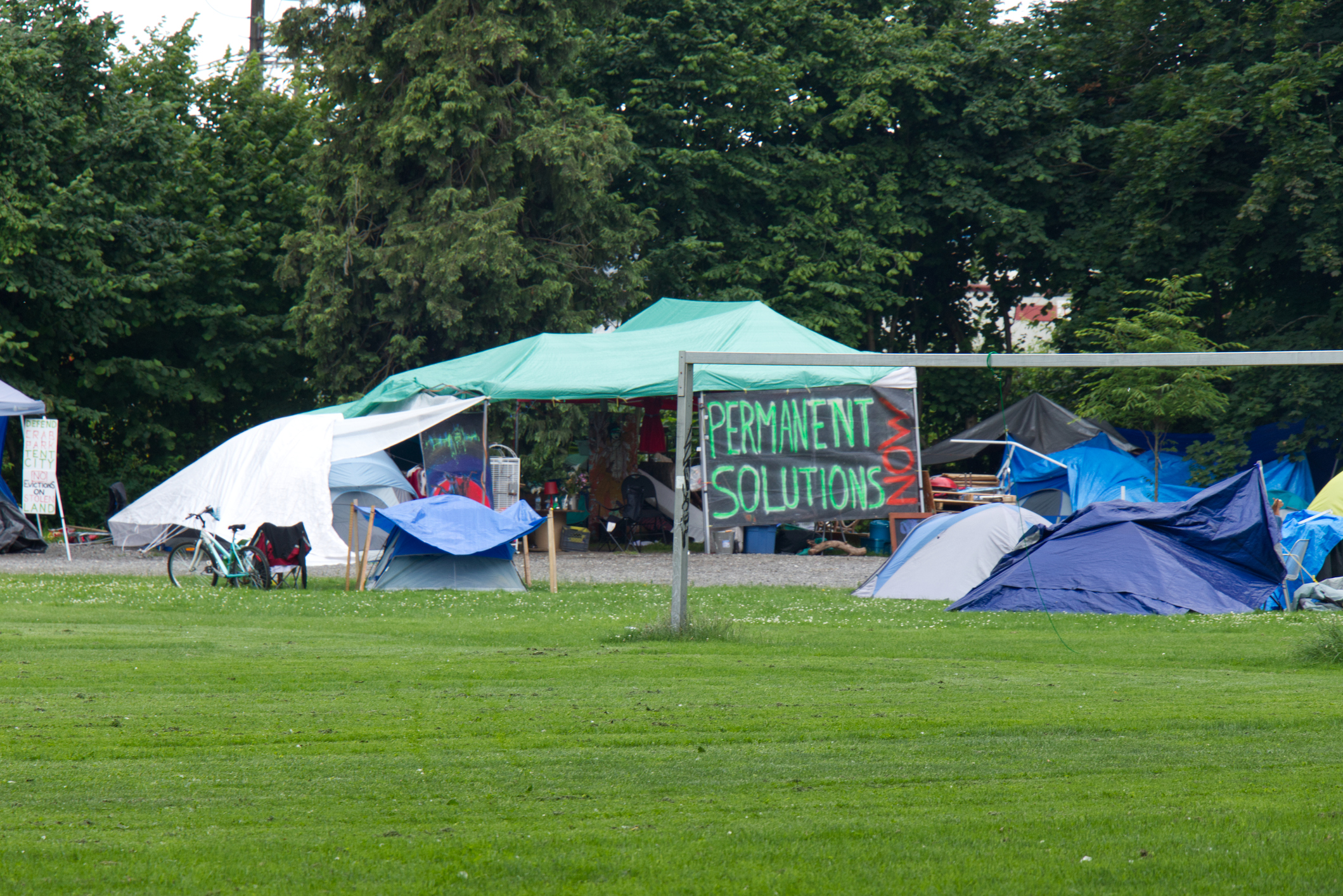 Vancouver, Canada - July 4, 2020: View of Strathcona Park in downtown Vancouver full of tents and homeless people with sign "Permanent solutions now" in the background